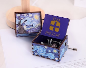 Puede incluir: Una caja de música de madera con un diseño de noche estrellada azul y blanca. La tapa está abierta y presenta una estrella dorada y las palabras "My Star".