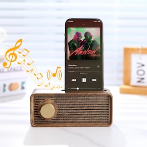 May include: A vintage-look wooden speaker with a gold control knob, holding a smartphone. The phone screen shows the music app playing "Attention" by Omah Lay & Justin Bieber. Musical notes are illustrated.