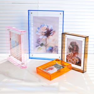 Pode incluir: Uma cole&ccedil;&atilde;o de molduras de fotos de acr&iacute;lico em v&aacute;rias cores e tamanhos. As molduras incluem rosa, azul, laranja e &acirc;mbar. Cada moldura cont&eacute;m uma imagem diferente, incluindo uma rosa em aquarela e um retrato de uma pessoa segurando flores.
