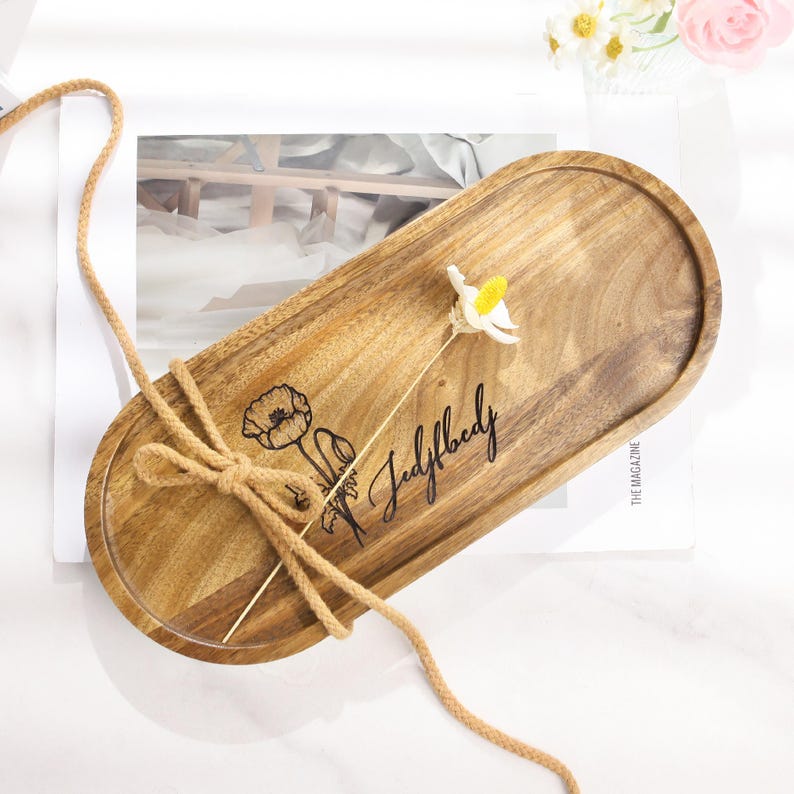 Op de afbeelding: Een ovaal houten dienblad met een lichtbruine afwerking. De lade heeft een bloemenontwerp en de tekst "Judylbody" in het hout ge&euml;tst. Een decoratief koord is om de lade gebonden. Een kleine bloem is op de lade geplaatst.
