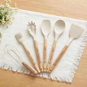 K&ouml;nnte beinhalten: Ein Set aus sechs K&uuml;chenutensilien, darunter ein Schneebesen, ein Pinsel, ein Spatel, ein L&ouml;ffel und eine Nudelkelle. Jedes Utensil hat einen hellbeigen Kopf und einen Holzgriff. Der Text "Cathy's Kitchen" ist auf jedem Griff aufgedruckt.