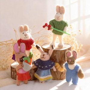 Könnte beinhalten: Eine Sammlung handgefertigter Hasenfiguren aus Filz. Jeder Hase trägt farbenfrohe Kleidung, darunter Pullover, Kleider und Overalls. Einige Hasen halten Karotten oder Blumen. Die Hasen werden auf kleinen Holzplattformen ausgestellt.