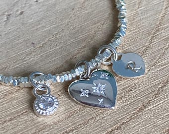 May include: A silver beaded bracelet with three charms. One charm is a heart with star and crystal accents. Another charm is a small round pendant with a single crystal. The third charm is a small heart with the letter "R".