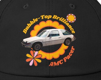 Może przedstawiać: Czarna, zniszczona czapka bejsbolowa z grafiką retro białego samochodu AMC Pacer. Projekt zawiera tekst "Bubble-Top Brilliance" i "AMC Pacer" w okrągłym wzorze z akcentami słońca i kwiatów.