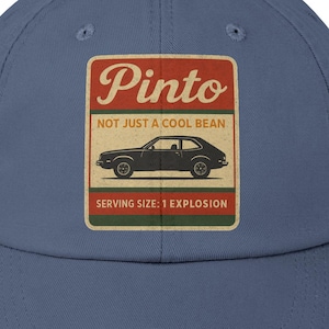 May include: A distressed blue baseball cap with a rectangular patch. The patch features the word "Pinto" in a vintage font, a car illustration, and the text "NOT JUST A COOL BEAN" and "SERVING SIZE: 1 EXPLOSION."
