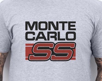 Może przedstawiać: Jasnoszara koszulka z napisem "MONTE CARLO" w czarnym kolorze nad czerwono-białym logo "SS". Koszulka ma okrągły dekolt i jest wykonana z miękkiego materiału.