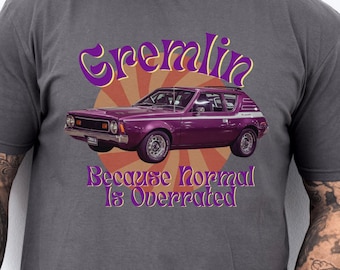 Może przedstawiać: Szary t-shirt z nadrukiem fioletowego samochodu AMC Gremlin i tekstem "Gremlin Because Normal Is Overrated".