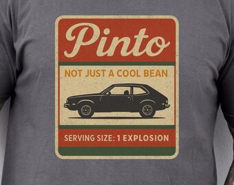 Może przedstawiać: Ciemnoszara koszulka z prostokątną grafiką. Grafika zawiera słowo "Pinto" w stylu vintage, frazę "NOT JUST A COOL BEAN" i ilustrację samochodu. Na dole grafiki widnieje napis "SERVING SIZE: 1 EXPLOSION."