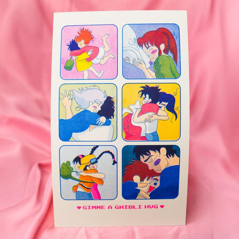 May include: A white card featuring six colorful illustrations of animated characters hugging. The phrase "Gimme a Ghibli Hug" is printed at the bottom in pink. The illustrations are in square frames.