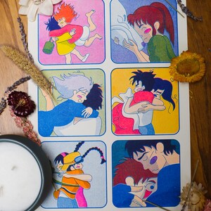 May include: A white poster with six colorful panels depicting animated characters hugging. The phrase "GIMME A GHIBLI HUG" is printed at the bottom in pink. The poster is surrounded by dried flowers and a candle.