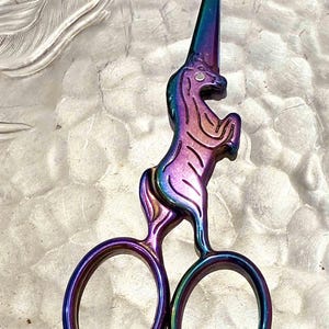 May include: A pair of iridescent rainbow-colored scissors shaped like a unicorn. The unicorn's horn is the top blade of the scissors.