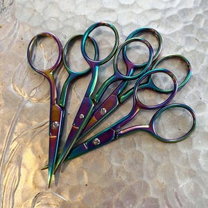 May include: Five pairs of small, rainbow-colored scissors with a metallic finish. The scissors are arranged in a fan shape, with the handles overlapping.