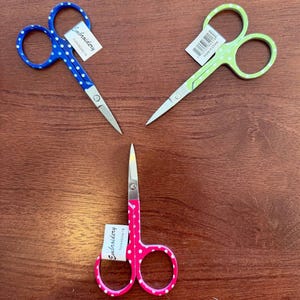 May include: Three pairs of small embroidery scissors with polka dot handles. The scissors are blue, green, and pink with white polka dots. Each pair has a label that says "Embroidery".