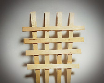 May include: A wooden lattice structure made of thin, light brown sticks. The sticks are arranged in a grid pattern, creating a series of squares.