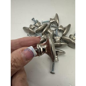 May include: A collection of silver-toned metal cabinet knobs with an oval-shaped front and a cylindrical base. Each knob features a threaded metal screw extending from the back for installation. The finish is smooth, reflective, and metallic.