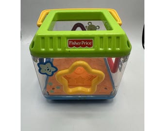 Cubo clasificador de formas Peek A Boo de Fisher Price con sonidos musicales para bebés y asa de transporte.