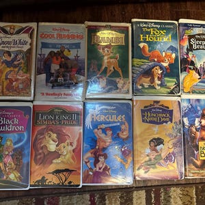 Könnte beinhalten: Eine Sammlung von Disney-VHS-Kassetten mit Zeichentrickklassikern wie "Schneewittchen", "Bambi", "Cap und Capper" und "Dornröschen". Die Kassetten befinden sich in ihrer Originalverpackung mit farbenfrohen Illustrationen.