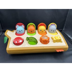 May include: A colorful, interactive toy featuring a wooden-look base with pop-up animal characters. Includes a blue mouse, orange fox, yellow chick, and gray bear. Additional shapes include a red mushroom, green leaf, orange flower, and yellow butterfly.