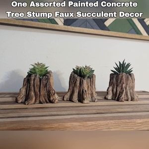 May include: Three faux succulent plants in painted concrete tree stump planters. The planters are brown and have a rustic wood grain texture. The plants are green and have a variety of shapes and sizes.