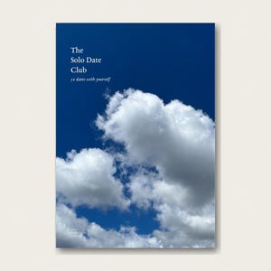 May include: A rectangular book cover featuring a deep blue sky filled with white, fluffy clouds. The text on the cover reads, The Solo Date Club, 52 dates with yourself, printed in a clean, white, serif font in the upper left corner.