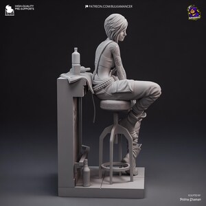 Puede incluir: Figura impresa en 3D de una persona sentada en un taburete detr&aacute;s de una barra. La persona tiene tatuajes en el brazo y lleva una camiseta sin mangas, un mono y botas. Hay botellas y una toalla en la barra. La figura es de color neutro.