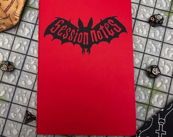 Puede incluir: Un cuaderno rojo con las palabras "Session Notes" en un diseño en forma de murciélago. El cuaderno está rodeado de dados y una bolsa de dados, lo que sugiere un tema de juego de mesa. La portada es de un rojo sólido y vibrante.