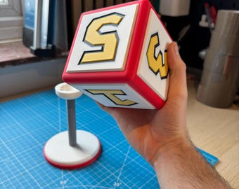 Op de afbeelding: Een rode, witte en gele kubus met de letters "S", "W" en "T" op elke zijde. De kubus wordt in de hand van een persoon gehouden.