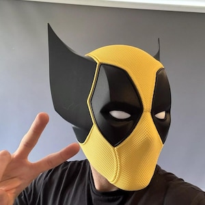 Könnte beinhalten: Eine gelbe und schwarze Deadpool-Maske mit strukturierter Oberfläche. Die Maske hat eine spitze Form mit zwei schwarzen Ohren.