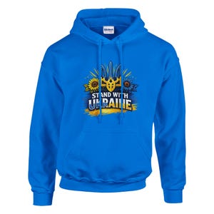 Könnte beinhalten: Kornblumenblauer Kapuzenpullover mit Frontaufdruck. Das Design zeigt das ukrainische Wappen, Sonnenblumen und den Text "STAND WITH UKRAINE". Der Hoodie hat eine Kapuze mit Kordelzug und eine Vordertasche.