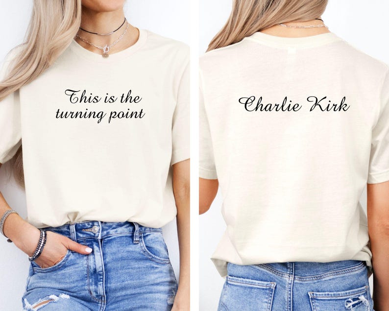 May include: Cream-colored t-shirt with the text "This is the turning point" on the front and "Charlie Kirk" on the back. The shirt is paired with blue jeans. The t-shirt has short sleeves and a crew neck.