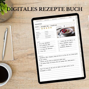 May include: A digital recipe book displayed on a tablet, showing a breakfast recipe with a photo of oatmeal and berries. The tablet is on a wooden surface, with a notepad, pen, coffee cup, and a plant in a silver pot. The text "DIGITALES REZEPTE BUCH" is at the top.