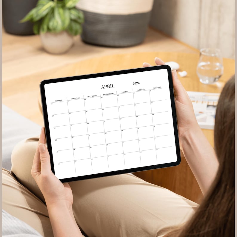 May include: A person is holding a tablet displaying a blank April 2026 calendar.
