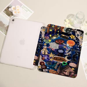 May include: A clear iPad case with a colorful, patterned insert featuring a collage of illustrations and the name "Coraline." The insert has a dark blue background with stars, buttons, and character figures. The iPad is white with the Apple logo.