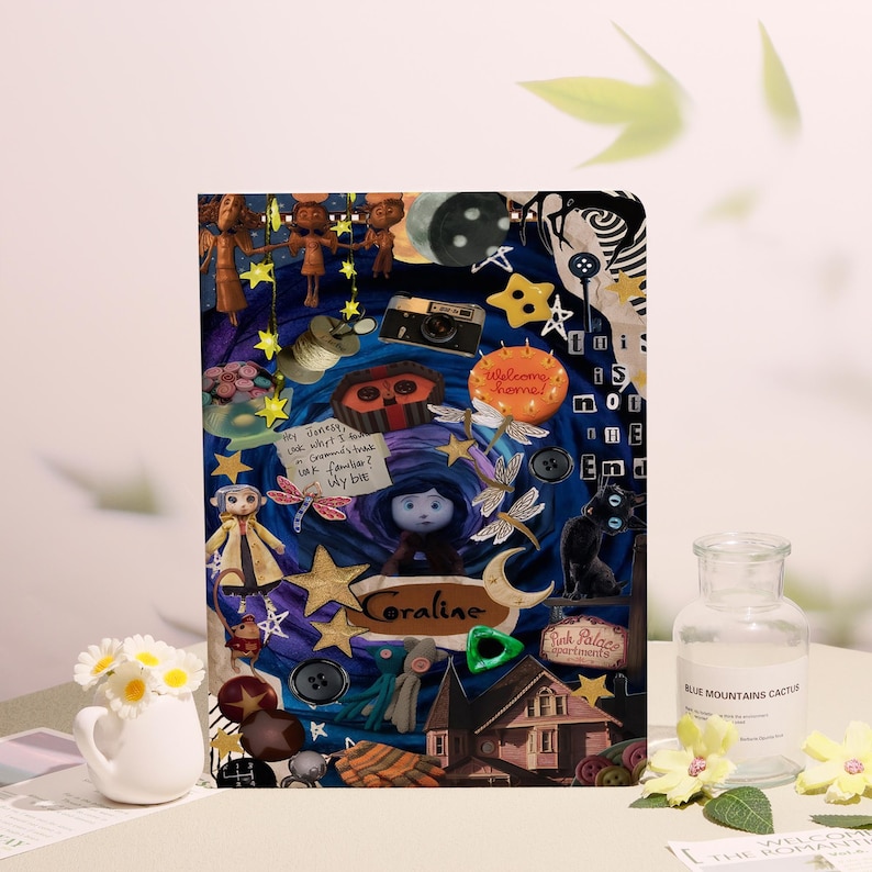May include: A decorative notebook featuring a collage of elements from the movie "Coraline." The design includes stars, buttons, a black cat, and the word "Coraline." The background is a mix of blue and purple.