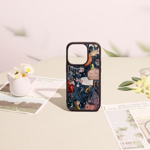 May include: A dark blue smartphone case featuring a collage of illustrations including a character with blue hair, a sign reading Pink Palace apartments, a key, scissors, a dragonfly, stars, and a house, all set against a starry night sky background.