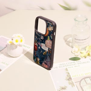 May include: A dark-themed phone case featuring a collage of illustrations including a character in a yellow raincoat, a house, a sign reading Pink Palace apartments, scissors, and various celestial elements against a deep blue starry background.
