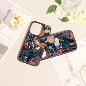 May include: Two dark blue phone cases featuring a detailed collage print of various objects including a small doll, scissors, a red tent, a pink sign reading Pink Palace Apartments, and star-shaped lights against a starry night sky background.