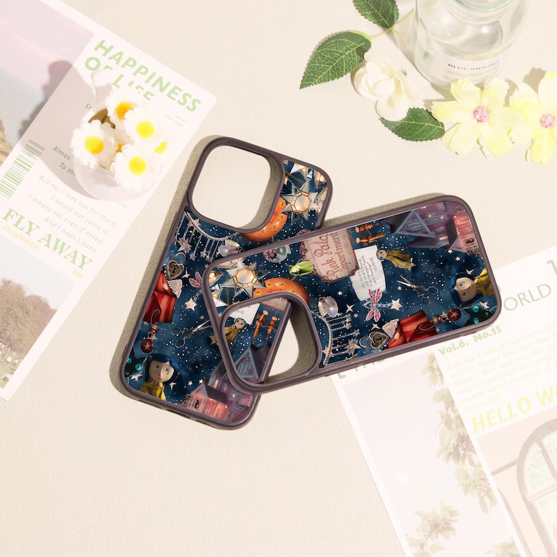 May include: Two dark blue phone cases featuring a detailed collage print of various objects including a small doll, scissors, a red tent, a pink sign reading Pink Palace Apartments, and star-shaped lights against a starry night sky background.