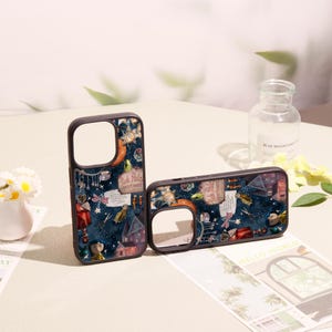 May include: Two dark-rimmed phone cases featuring a deep blue night sky pattern with various illustrated icons, including a house, stars, a dragonfly, and a sign that reads Pink Palace apartment, with cutouts for the camera lens.