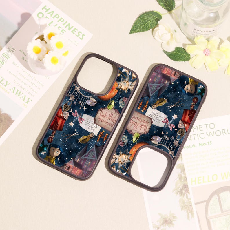 May include: Two dark-rimmed phone cases featuring a dark blue starry night background with various illustrated elements including a house, a sign reading Pink Palace apartment, a small doll figure, scissors, and a key against a starry sky.