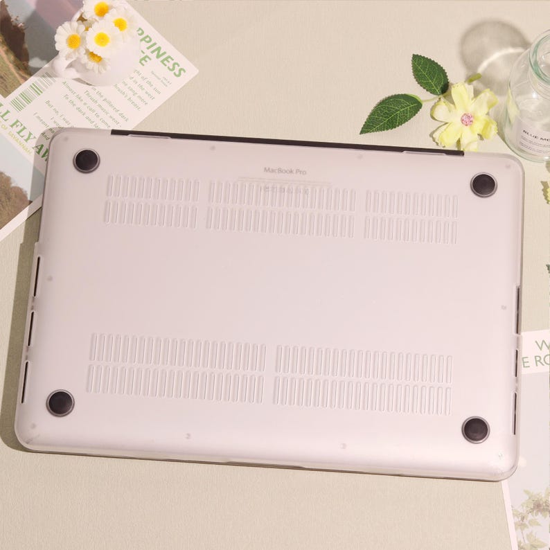May include: A clear, protective case for a MacBook Pro laptop. The case is transparent, allowing the laptop's color to show through. The bottom of the case has ventilation slots and rubber feet for stability. The text "MacBook Pro" is visible.