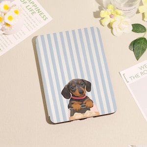 Peut inclure: Un étui rectangulaire à rayures bleues claires et blanches. Un dessin animé de teckel portant un collier rose est présenté sur l'étui. Le teckel est assis dans un récipient avec de la nourriture.