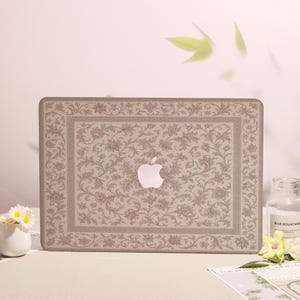 Peut inclure: Un autocollant pour ordinateur portable présentant un motif floral complexe de vignes beiges et brunes avec une bordure rectangulaire. Le design est centré autour d'une découpe pour le logo Apple blanc. Le motif se compose de feuilles et de fleurs.