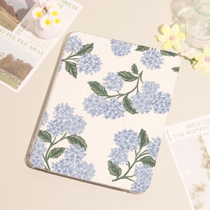 May include: A cream-coloured tablet case with a pattern of light blue hydrangea flowers and green leaves. The case is rectangular and has a smooth surface. The floral design is repeated across the entire surface.
