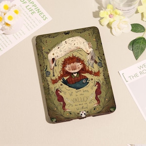 May include: A green tablet case featuring an illustration of a girl with red braids, a white wolf, and the text "We were born in the Valley of the dead and the Wicked." The case has a whimsical, storybook aesthetic.