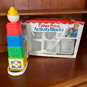 May include: A Fisher-Price Activity Blocks toy set. The set includes a stackable tower with red, blue, green, and yellow blocks, topped with a yellow egg. The box features the Fisher-Price logo and images of the toy.