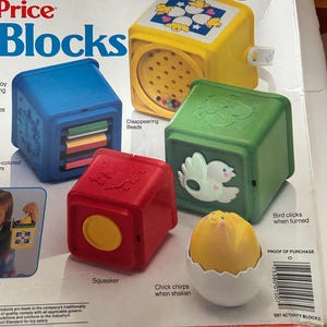 May include: A selection of Fisher-Price Blocks toys in various colours. The set features a blue block with sliding panels, a yellow block with a bead-filled window, a green block with a bird design, and a red block with a yellow circle. A yellow chick in a white egg is also included.