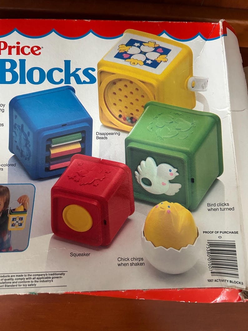 May include: A selection of Fisher-Price Blocks toys in various colours. The set features a blue block with sliding panels, a yellow block with a bead-filled window, a green block with a bird design, and a red block with a yellow circle. A yellow chick in a white egg is also included.