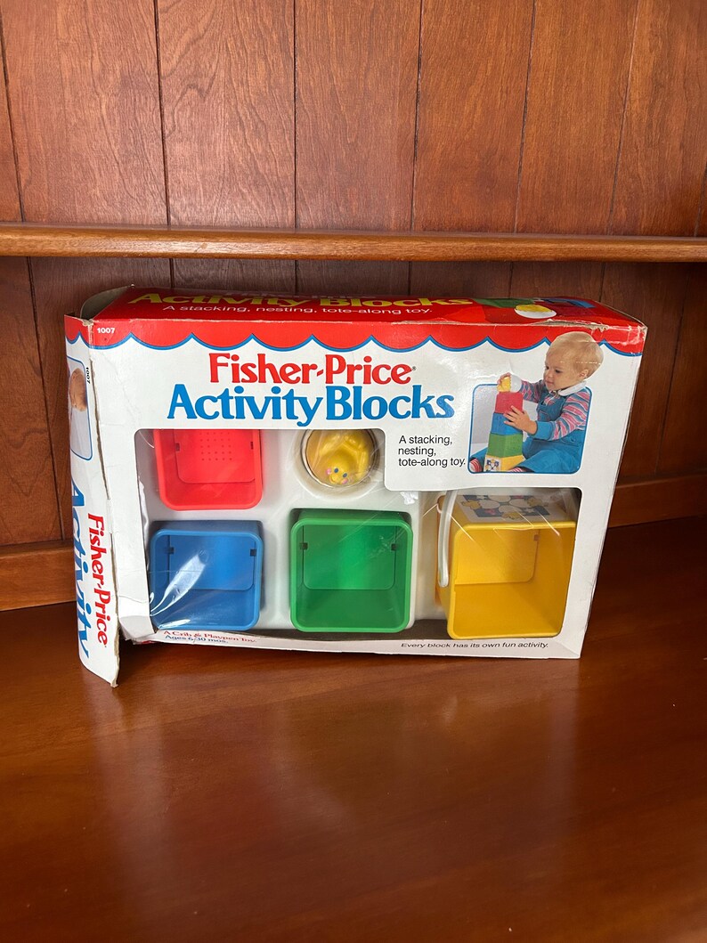 May include: A Fisher-Price Activity Blocks set in its original packaging. The box features a red and white design with the product name and a picture of a child playing with the blocks. The set includes red, blue, green, and yellow blocks.