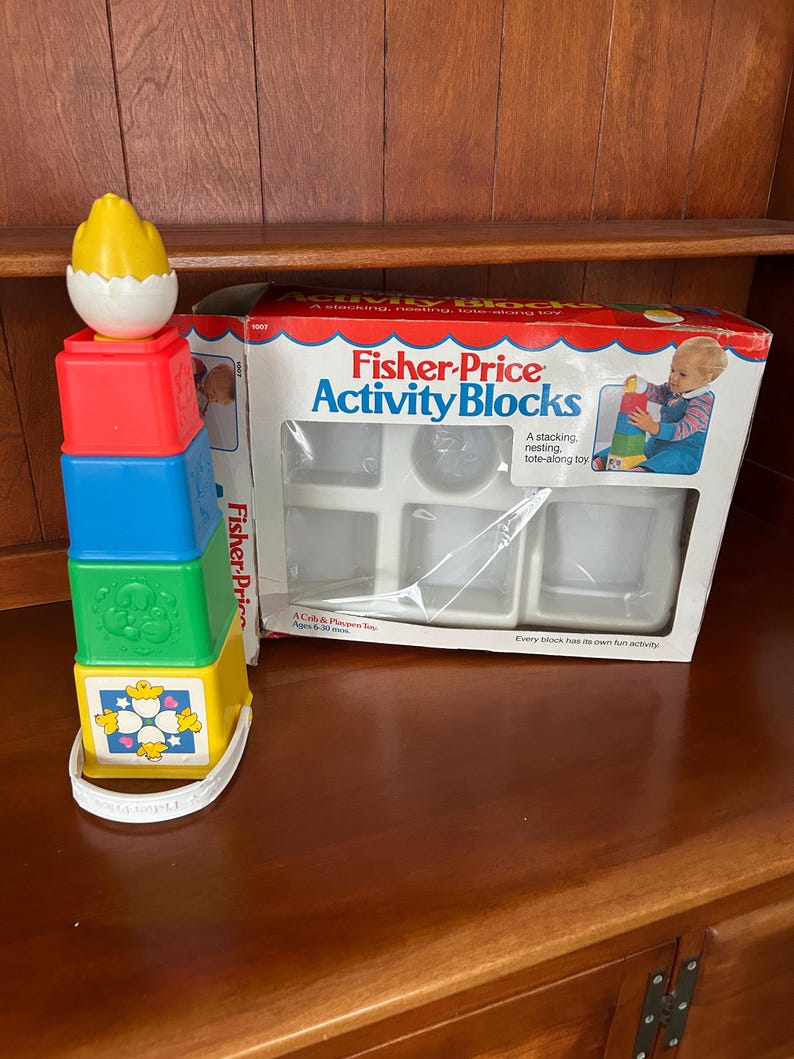 May include: A Fisher-Price Activity Blocks toy set. The set includes a stackable tower with red, blue, green, and yellow blocks, topped with a yellow egg. The box features the Fisher-Price logo and images of the toy.